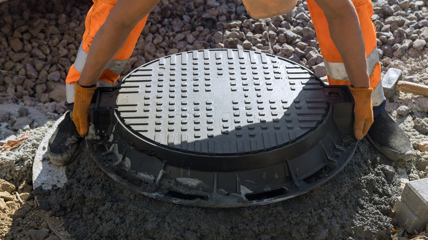 A manhole cover is being removed from the ground by a construction worker.
