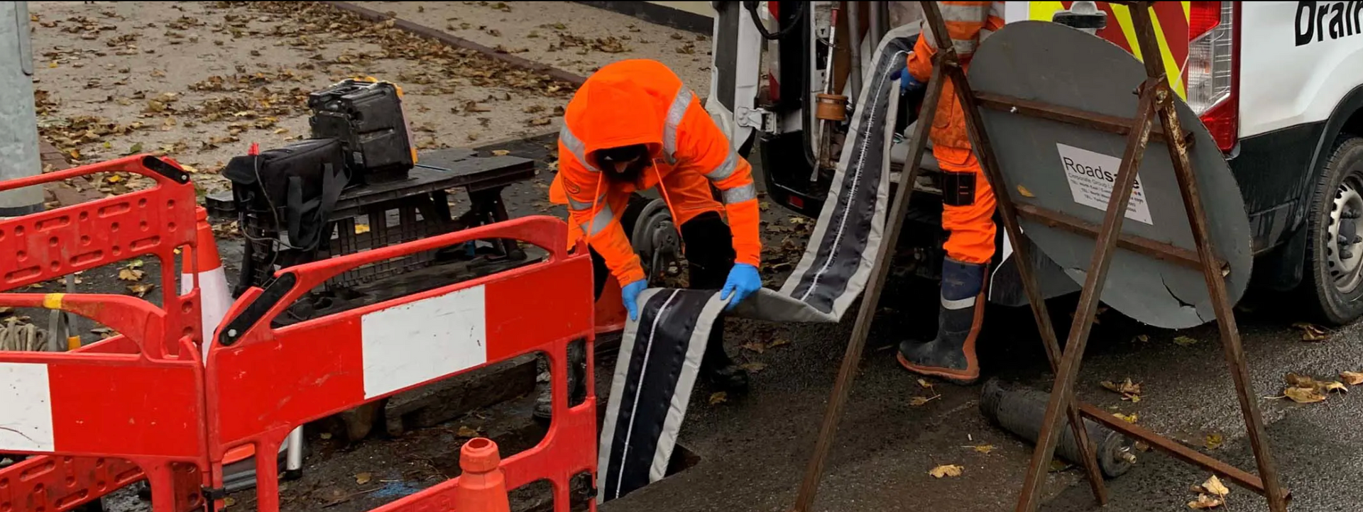 Workers in orange vests installing a road sign in a street.