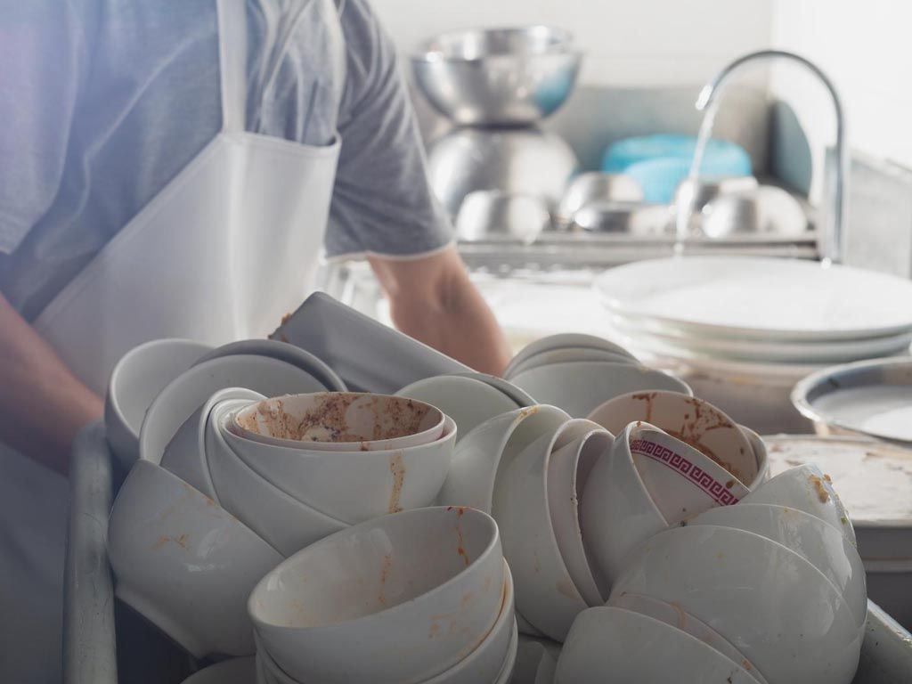 A man is holding a tray of dirty bowls in a kitchen.