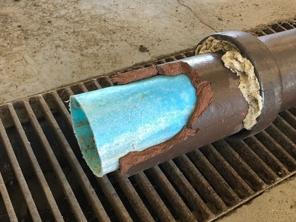 Cutaway view of a brown pipe revealing blue interior and insulation, resting on a metal grate.