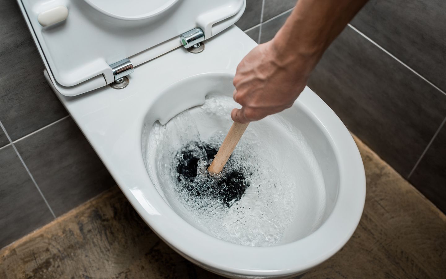 Person uses a plunger to unclog a toilet filled with water and bubbles.