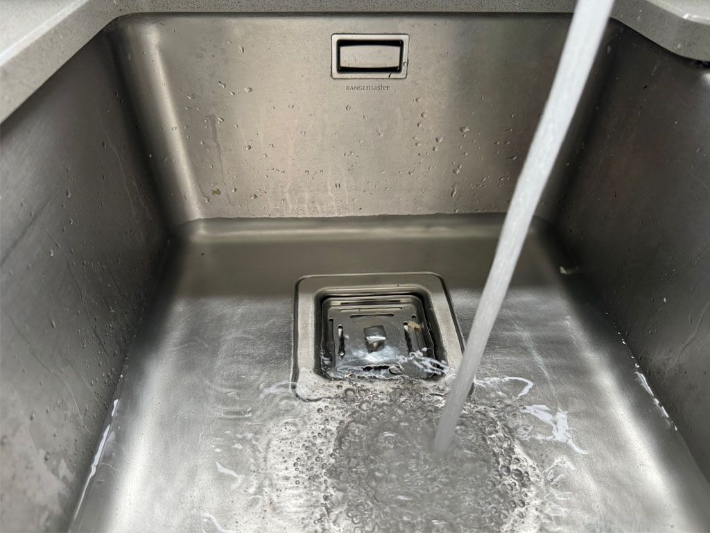 A faucet is pouring water into a stainless steel sink.