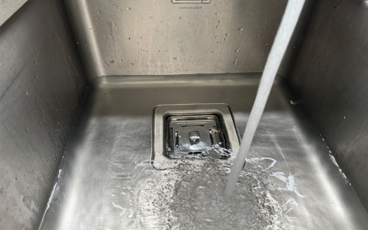 Water pouring into a stainless steel kitchen sink, overflowing slightly.