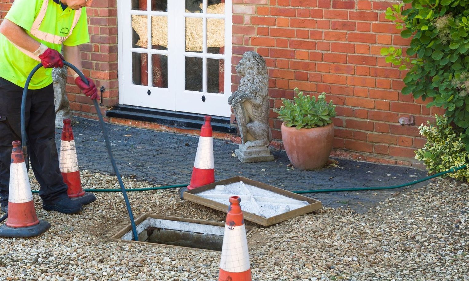 A professional drainage man is cleaning a drain outside of a house.