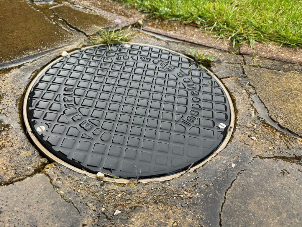 A manhole cover is sitting on a path next to a grassy area.