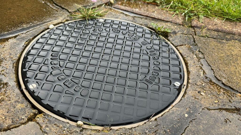 A manhole cover is sitting on a path next to a grassy area.