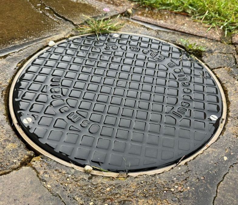 A manhole cover is sitting on a path next to a grassy area.