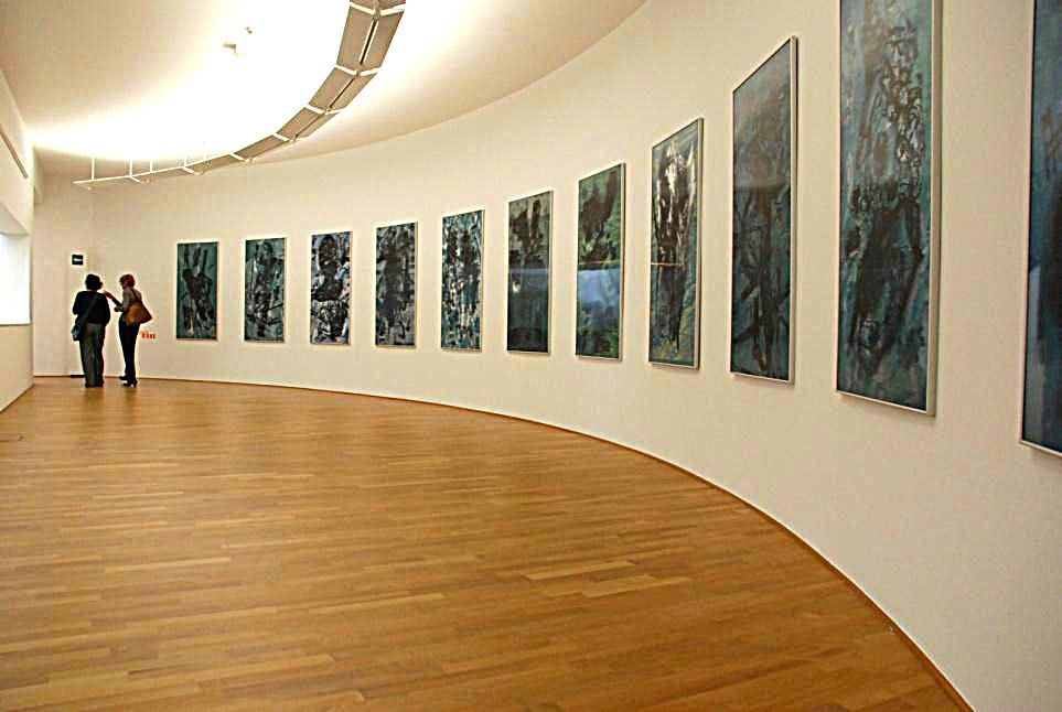 two people are looking at paintings on a wall in a museum .