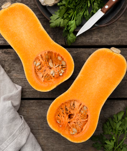 Calabaza cortada por la mitad, dejando al descubierto las semillas, sobre una mesa de madera con cuchillo y perejil.
