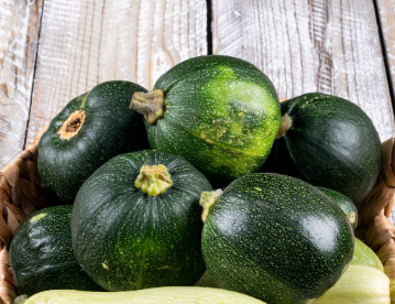 Cesta de calabacines redondos de color verde oscuro sobre un fondo de madera desgastada.