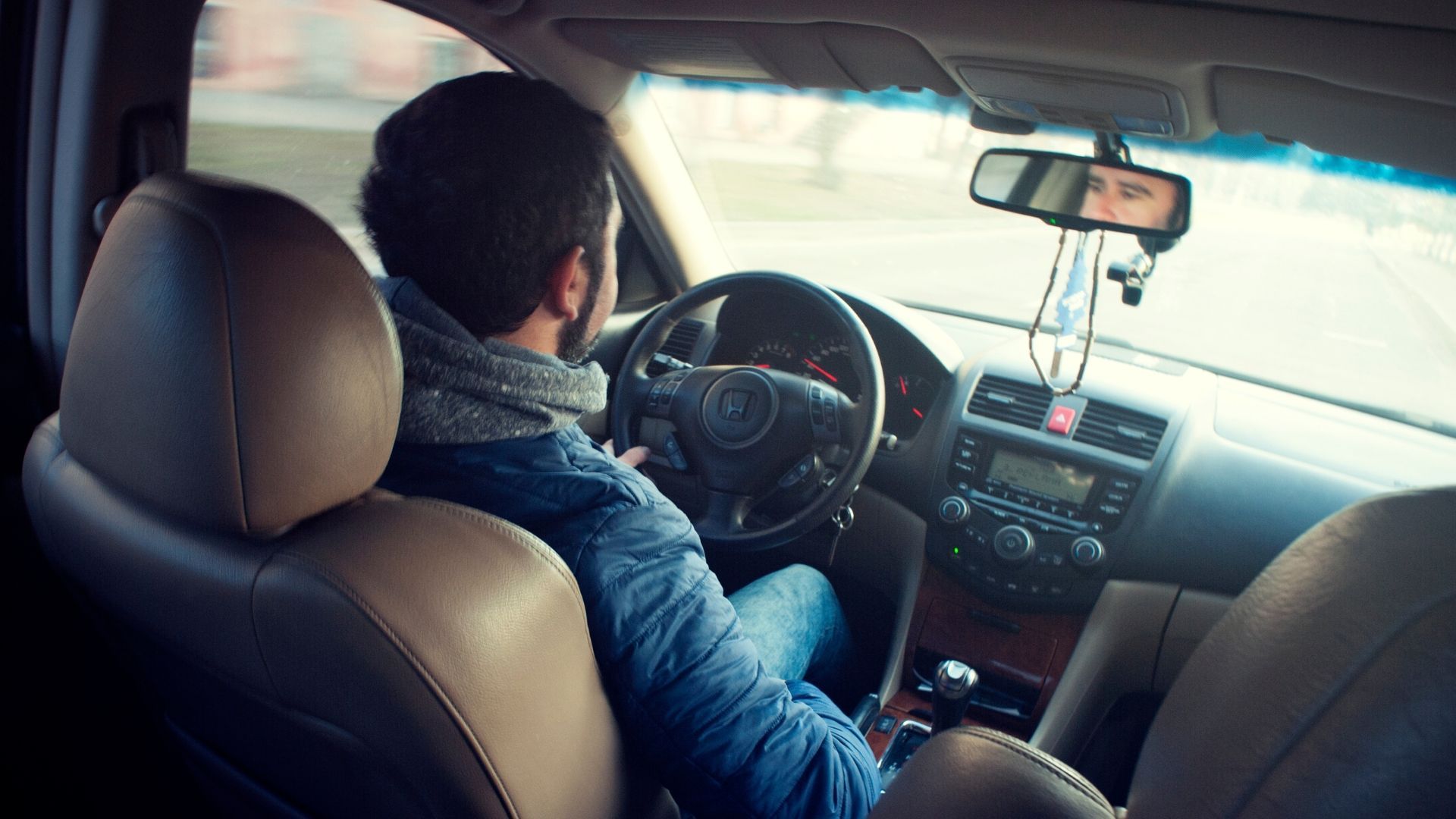 Driver seated in a car, hands on the wheel, driving on a bright road