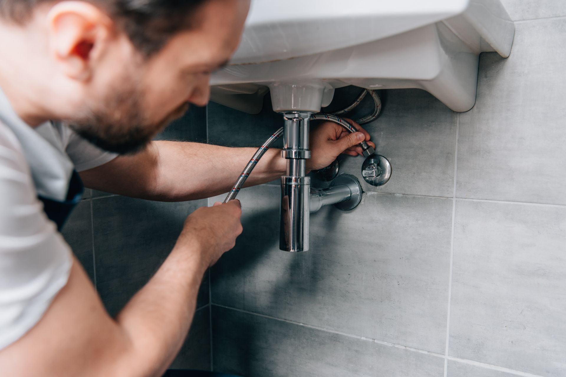 Plumber with a hose working under a bathroom sink.