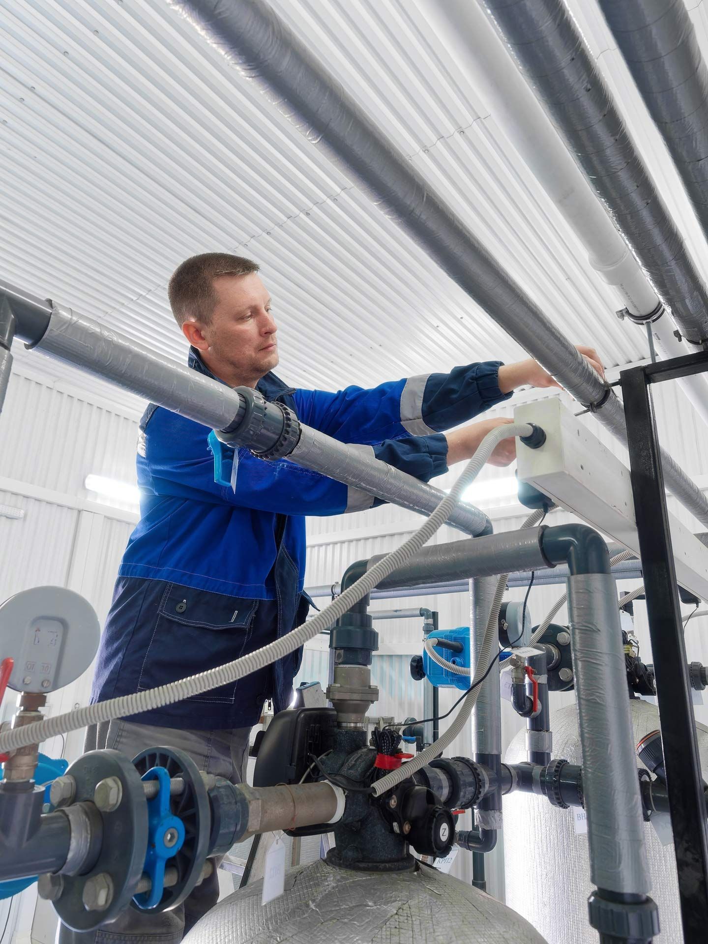 A middle-aged Caucasian plumber in overalls is repairing a water supply system