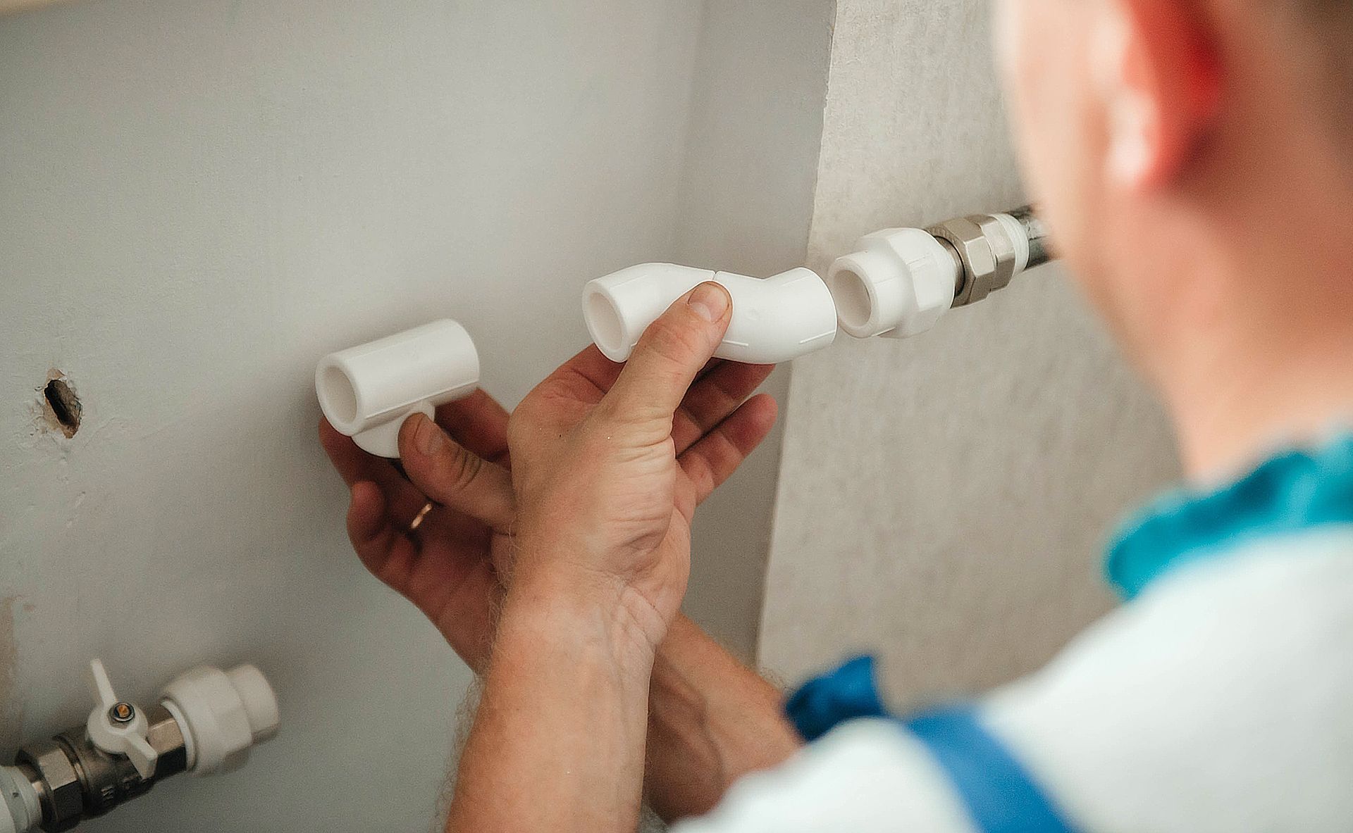 Person installing white plastic plumbing fittings on a wall pipe.