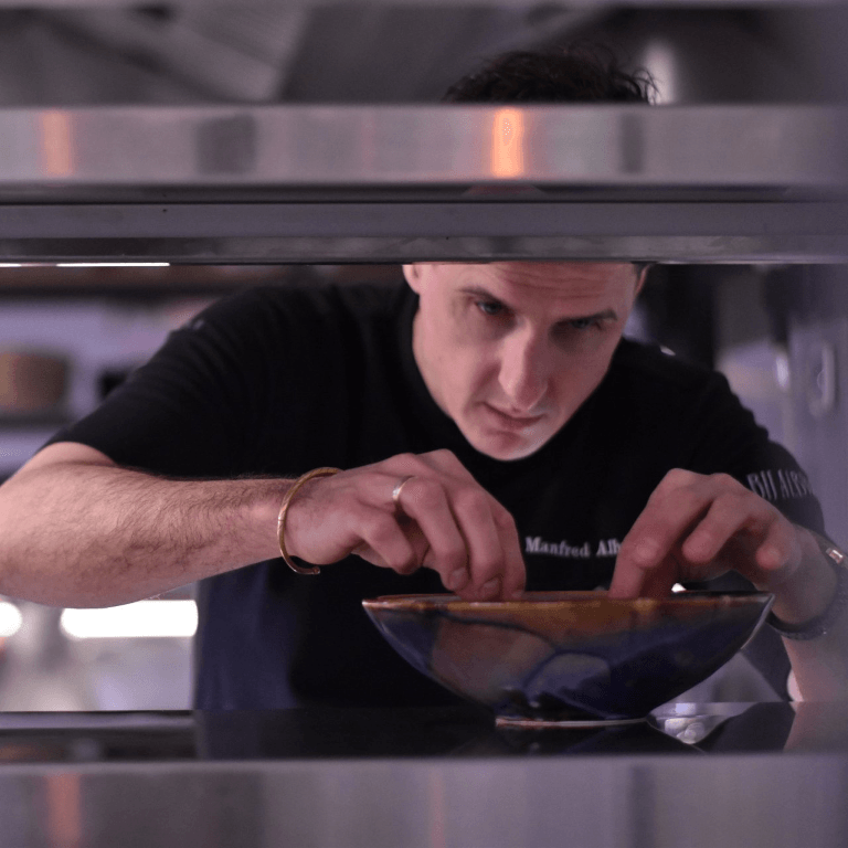 Een geconcentreerde chef-kok in een zwart uniform schikt zijn gerechten met precisie in een professionele keuken.