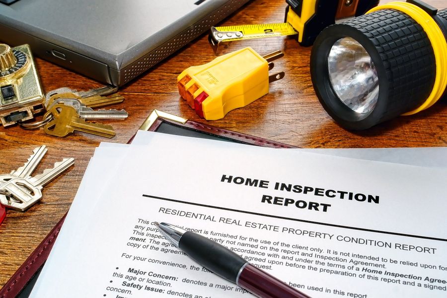 A home inspection report, pen, keys, flashlight, and tools on a wooden surface.