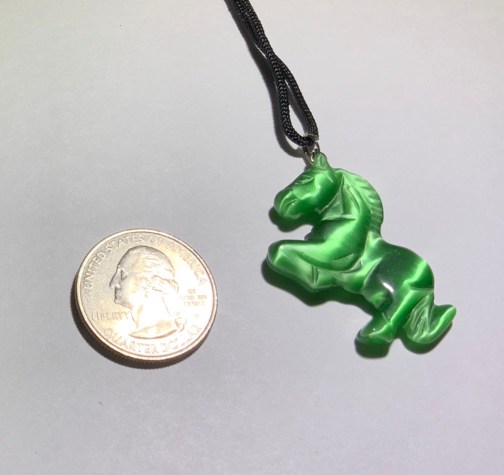 Green horse pendant next to a US Quarter
