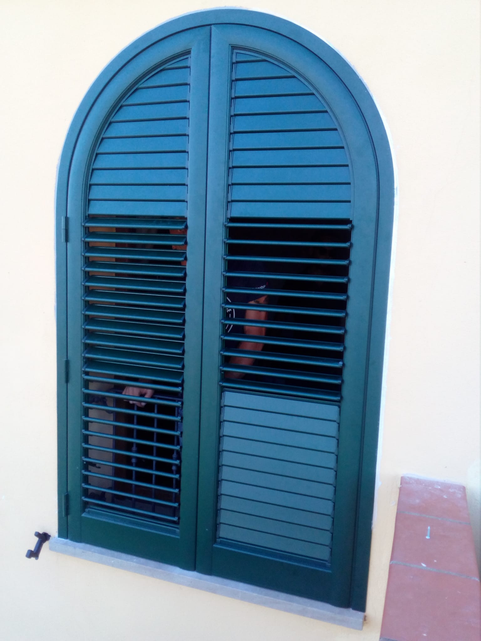 Persiane verdi ad arco su un edificio color crema.