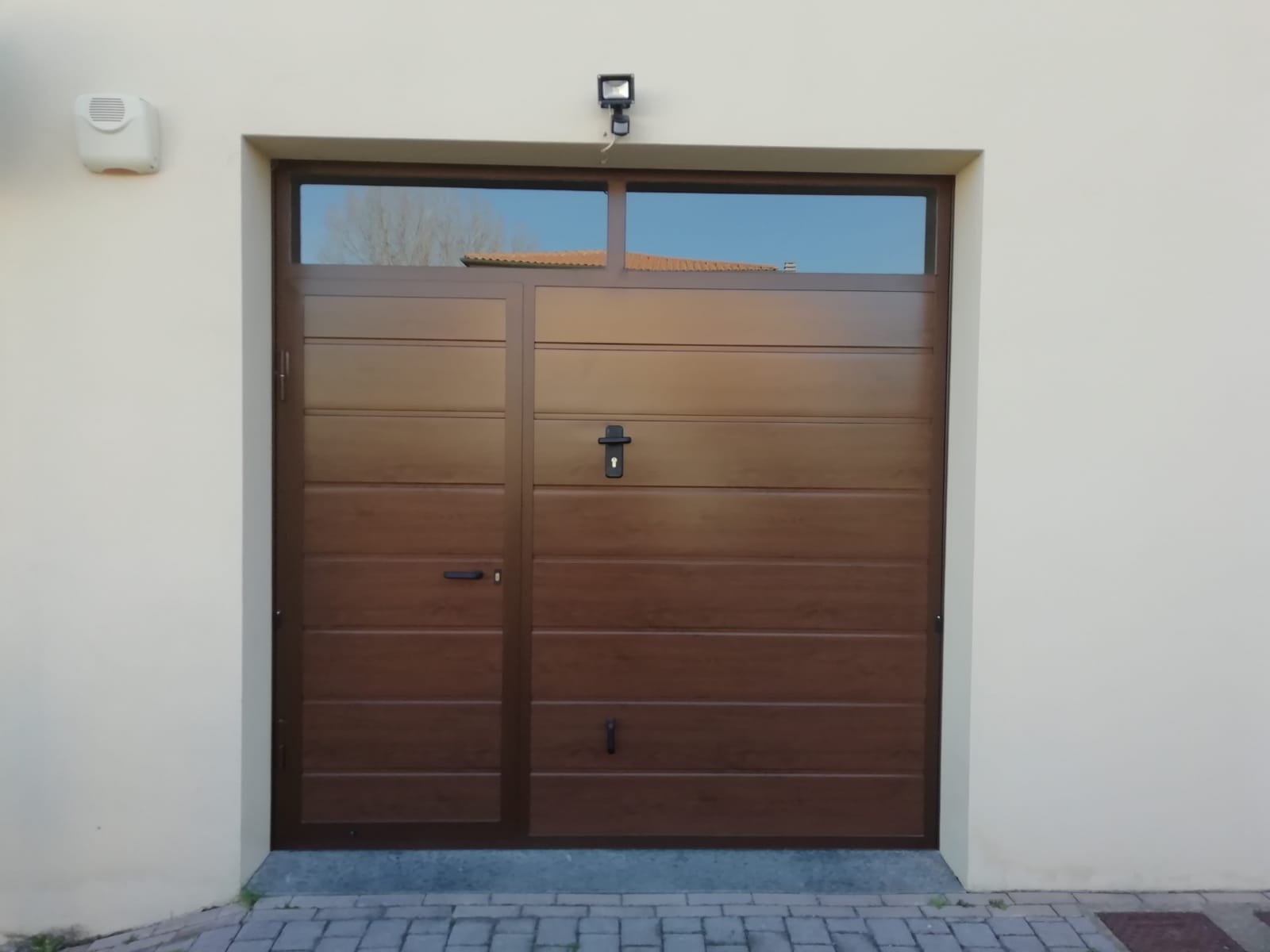 Porta da garage marrone con porta d'ingresso più piccola e finestra sopra. Luce in alto.