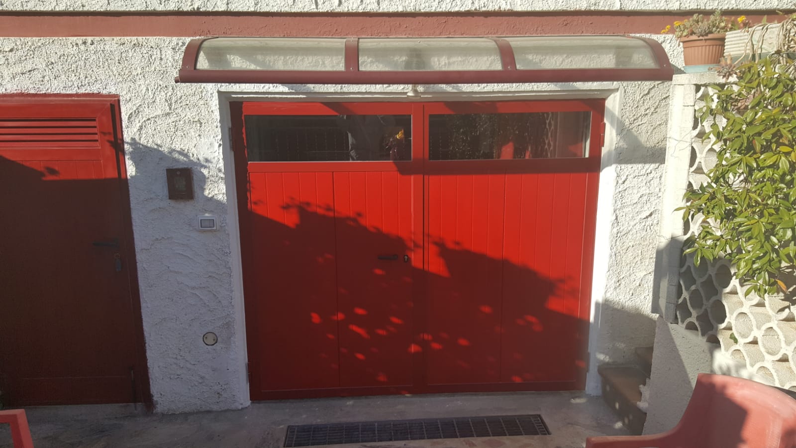 Porta da garage rossa con piccola tenda in vetro, inserita in una parete in stucco bianco.
