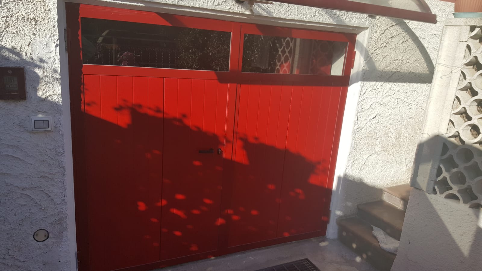Porta in legno rosso, anticata, con pannello in vetro sopra, inserita in una parete bianca testurizzata.