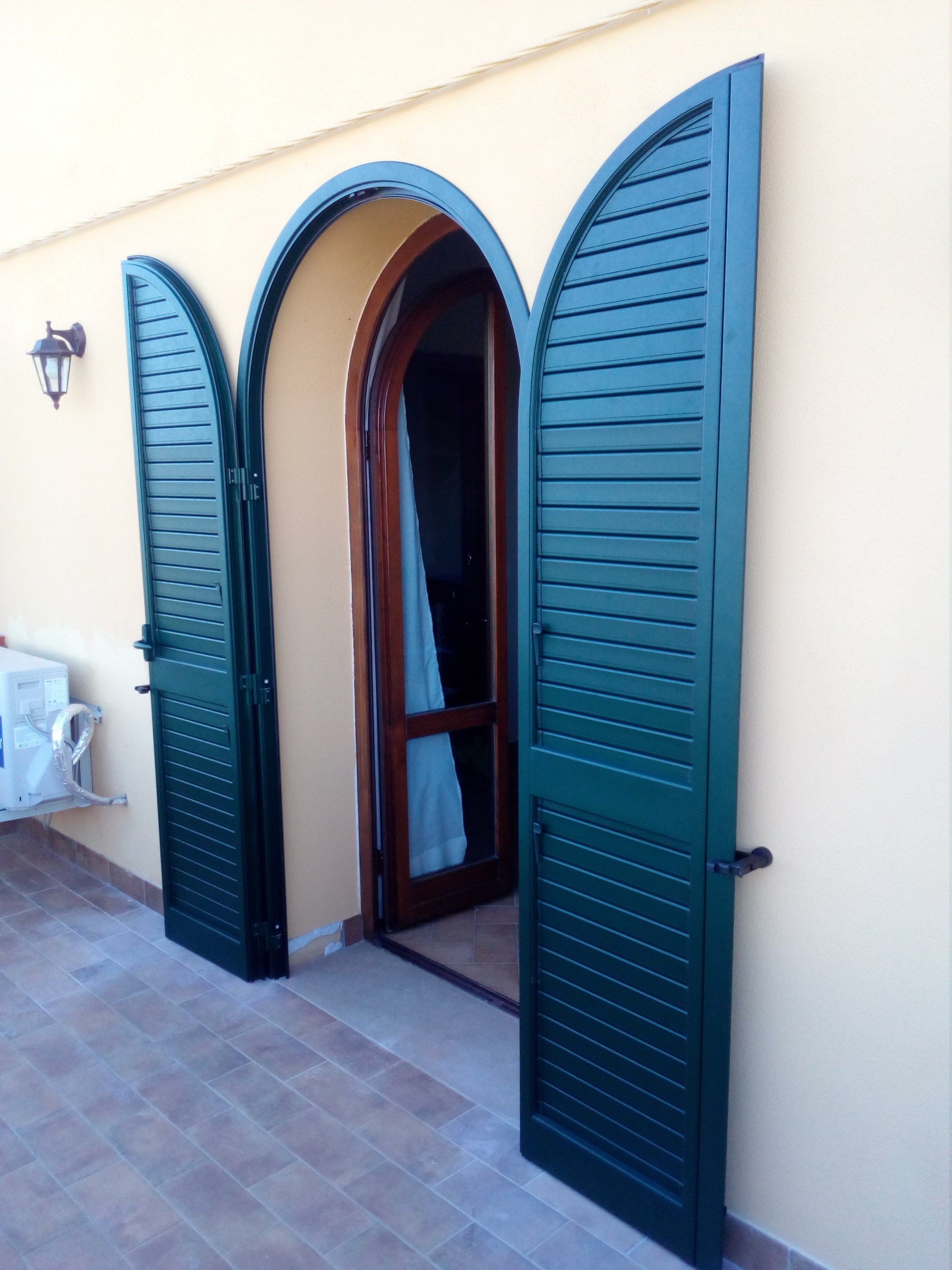 Persiane verdi si aprono su una porta ad arco, che conduce in una stanza. Pareti giallo chiaro.