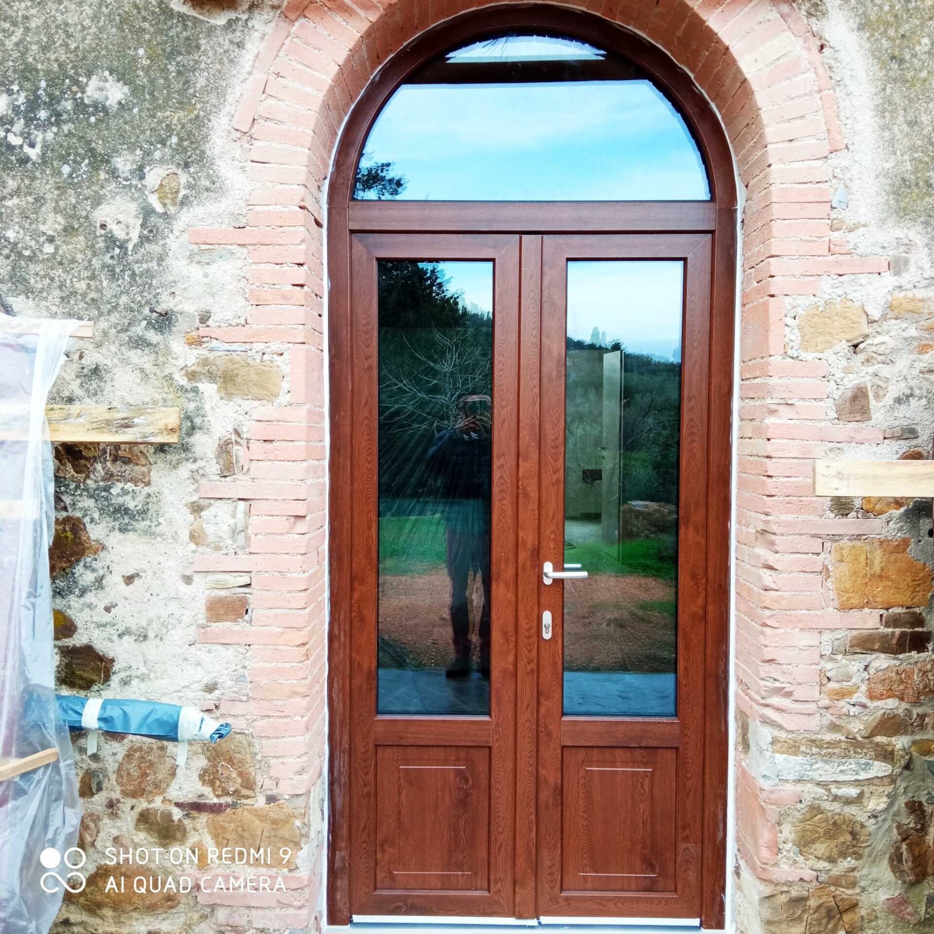 Porta doppia marrone con finestra ad arco inserita in un portale in mattoni e pietra.
