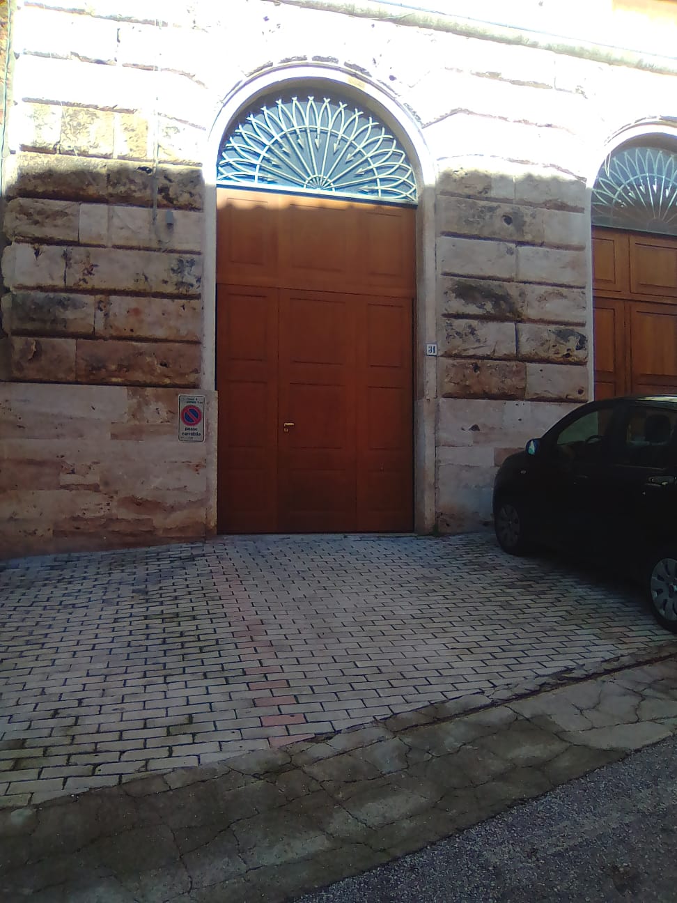 Grande porta marrone nella facciata di un edificio in pietra, con parte superiore ad arco e finestra decorata nella parte superiore.