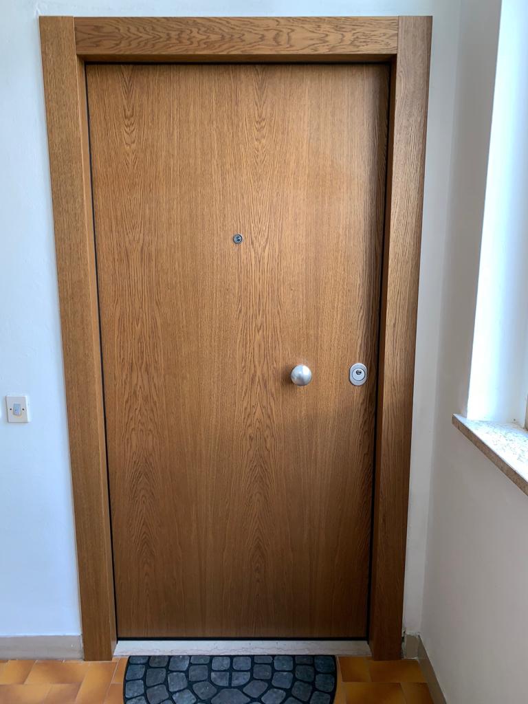 Porta di legno con maniglia, spioncino e cornice in un corridoio.