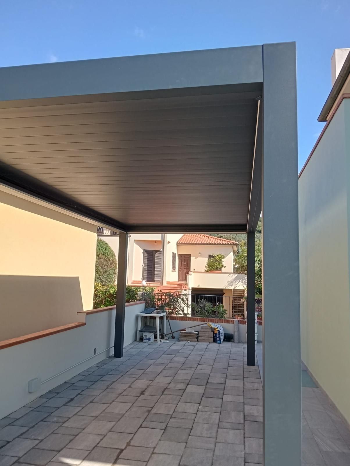 Vista attraverso le porte a vetri: patio esterno, corridoio interno con pavimento in legno, maniglia della porta bianca.