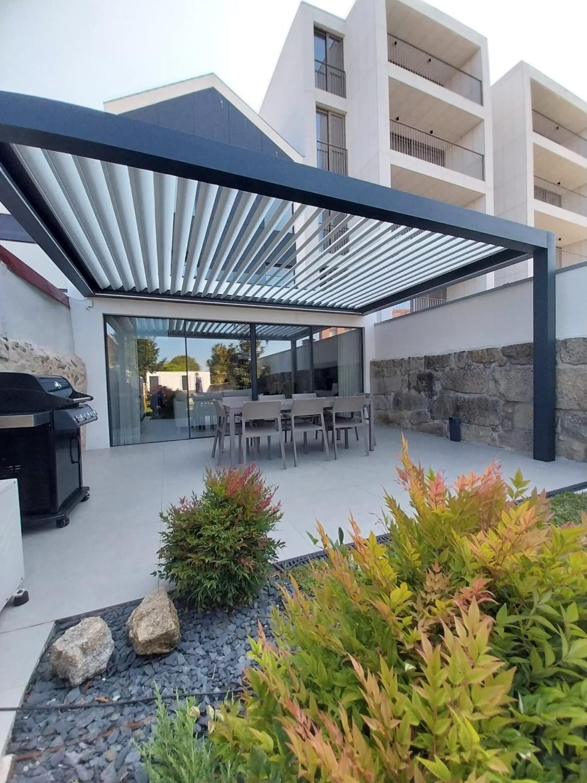 Patio esterno con sedie e tavolo verdi, piante in vaso e porta scorrevole in vetro.