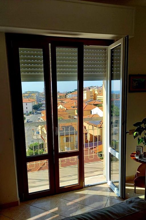 Finestra in legno marrone con doppi vetri inserita in una parete bianca; parzialmente aperta, riflette la vista esterna.