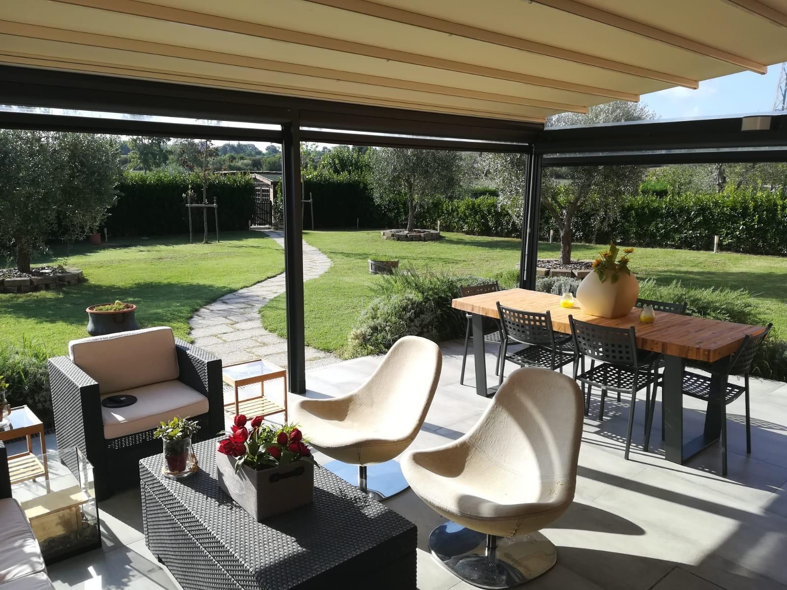 Pergola in legno con area salotto, barbecue e giardino lussureggiante nelle giornate di sole.