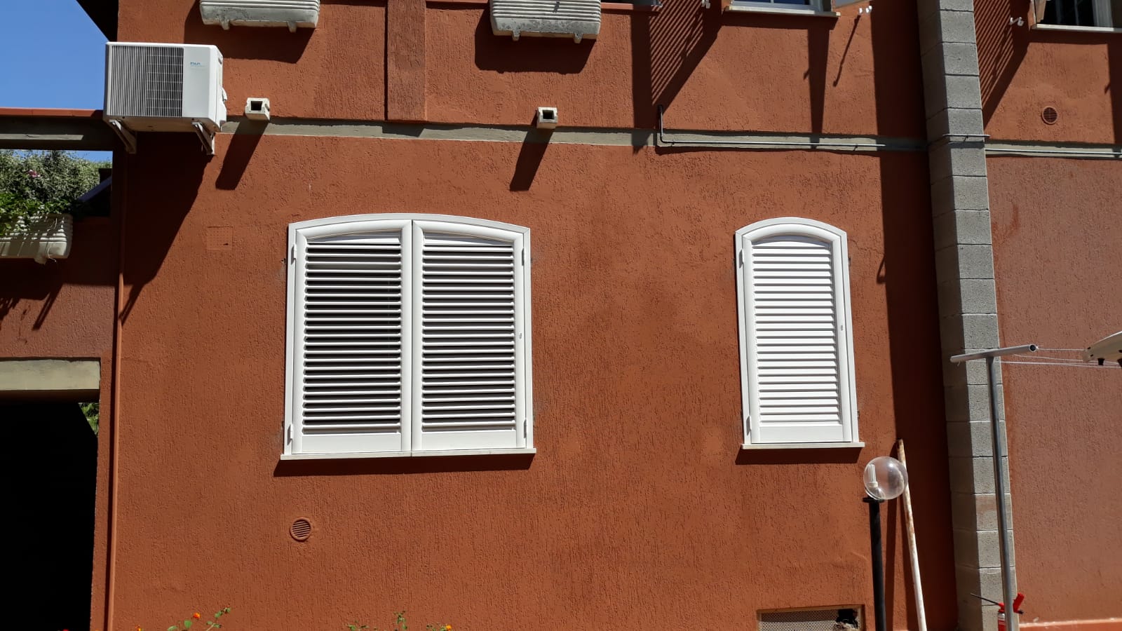 Facciata rossa dell'edificio con due finestre bianche con persiane e aria condizionata.