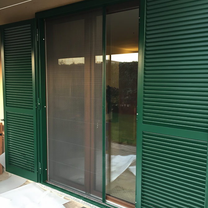 Persiane verdi e una porta a vetri con zanzariera che conduce a un cortile.