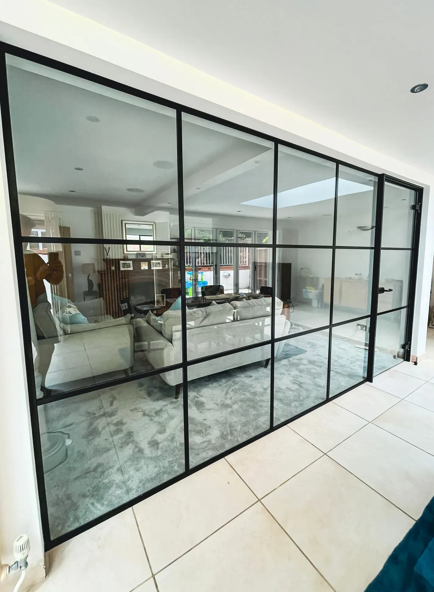 Black-framed glass doors separating two rooms; visible living room furniture and tile floor.