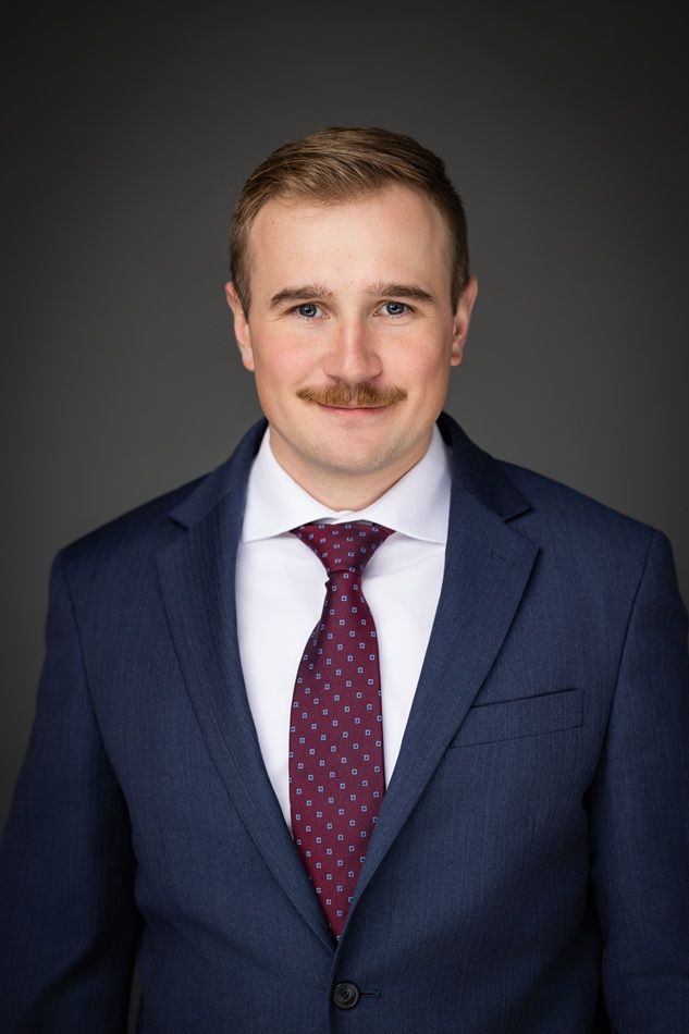 Man in a suit and tie, smiling, dark background.