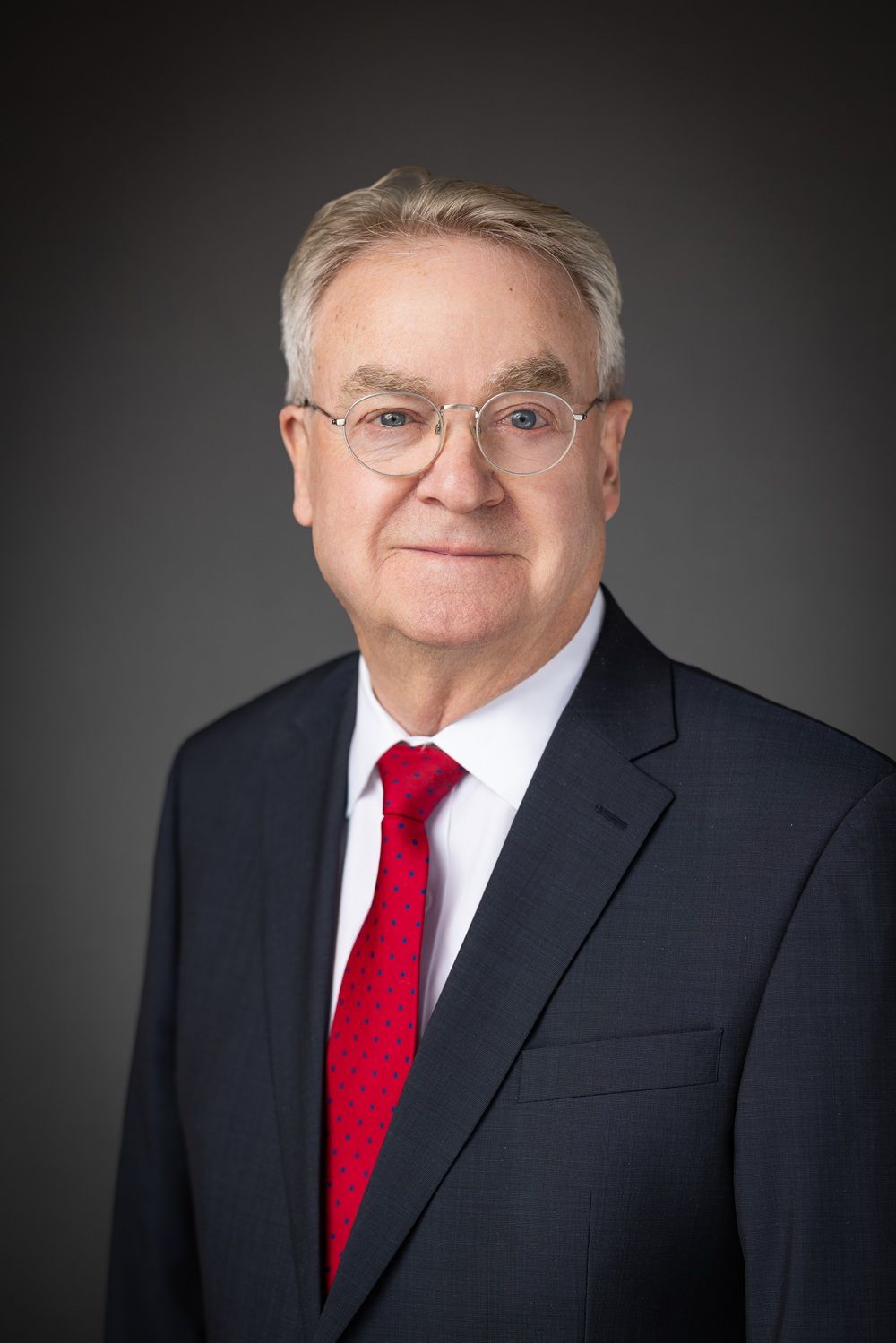 Man in suit and tie, wearing glasses, smiling, posed portrait.