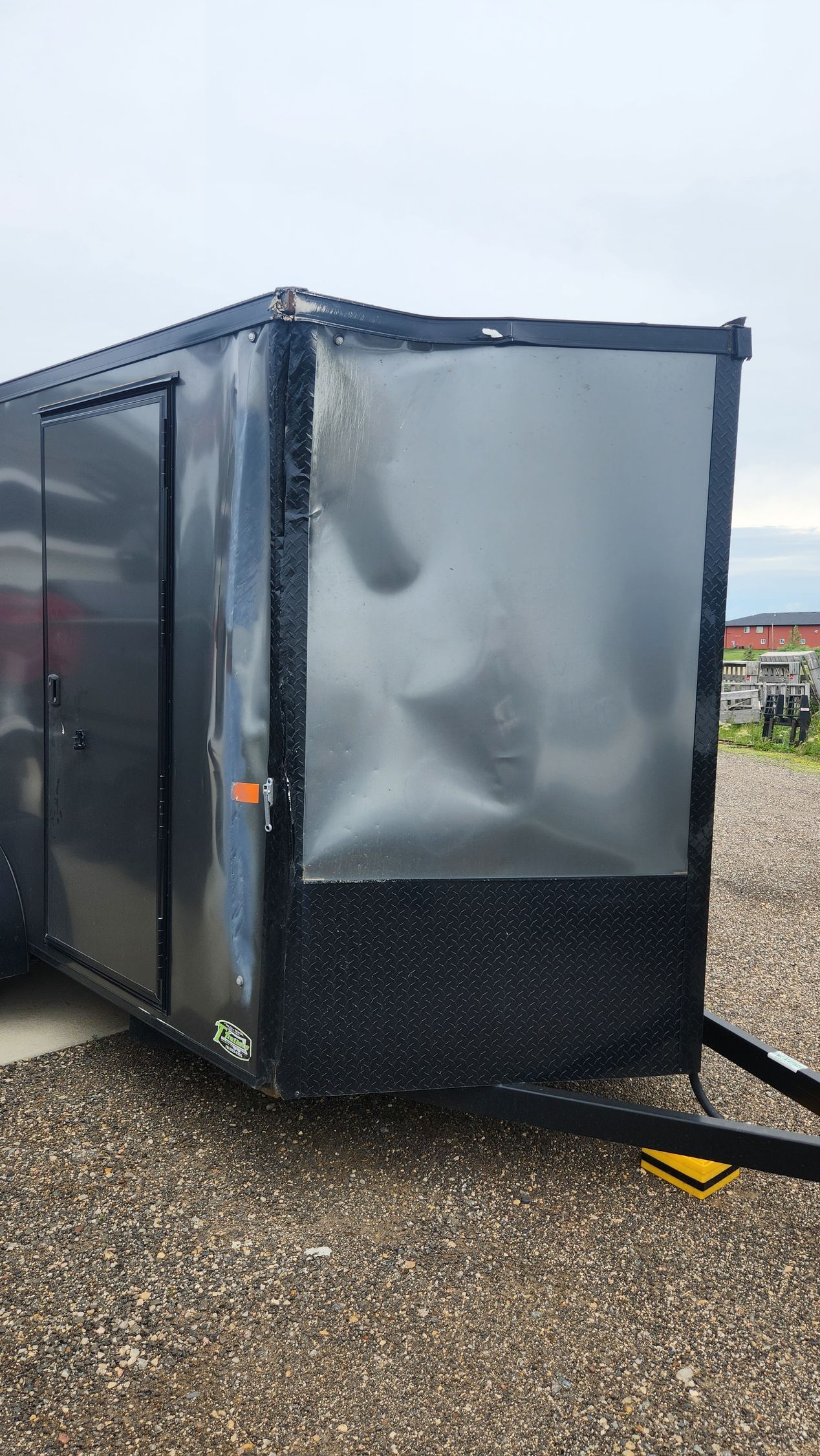 Black enclosed trailer with a reflective silver front panel on a gravel lot.