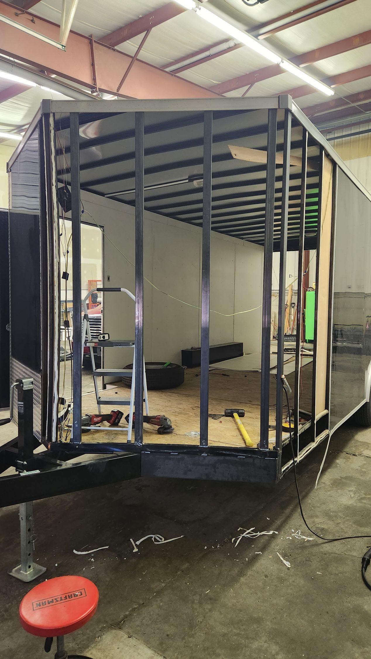 Partially built metal-framed trailer or container inside a workshop, with tools and materials around it.