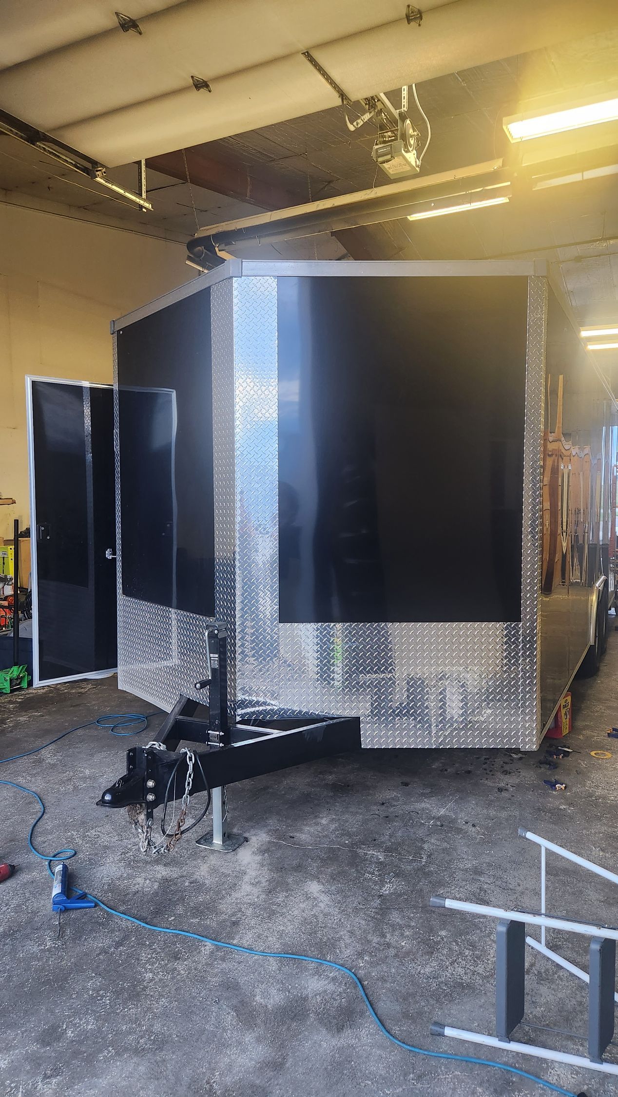 Large black trailer or equipment enclosure in a workshop, with reflective panels and tools on the floor.