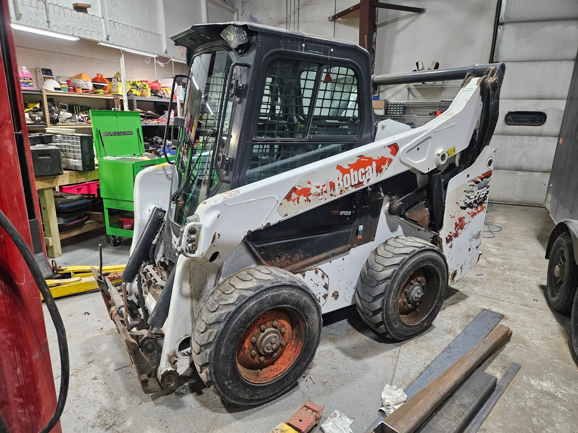 White Bobcat skid steer in a workshop, showing wear and rust, with tools and metal beams nearby.