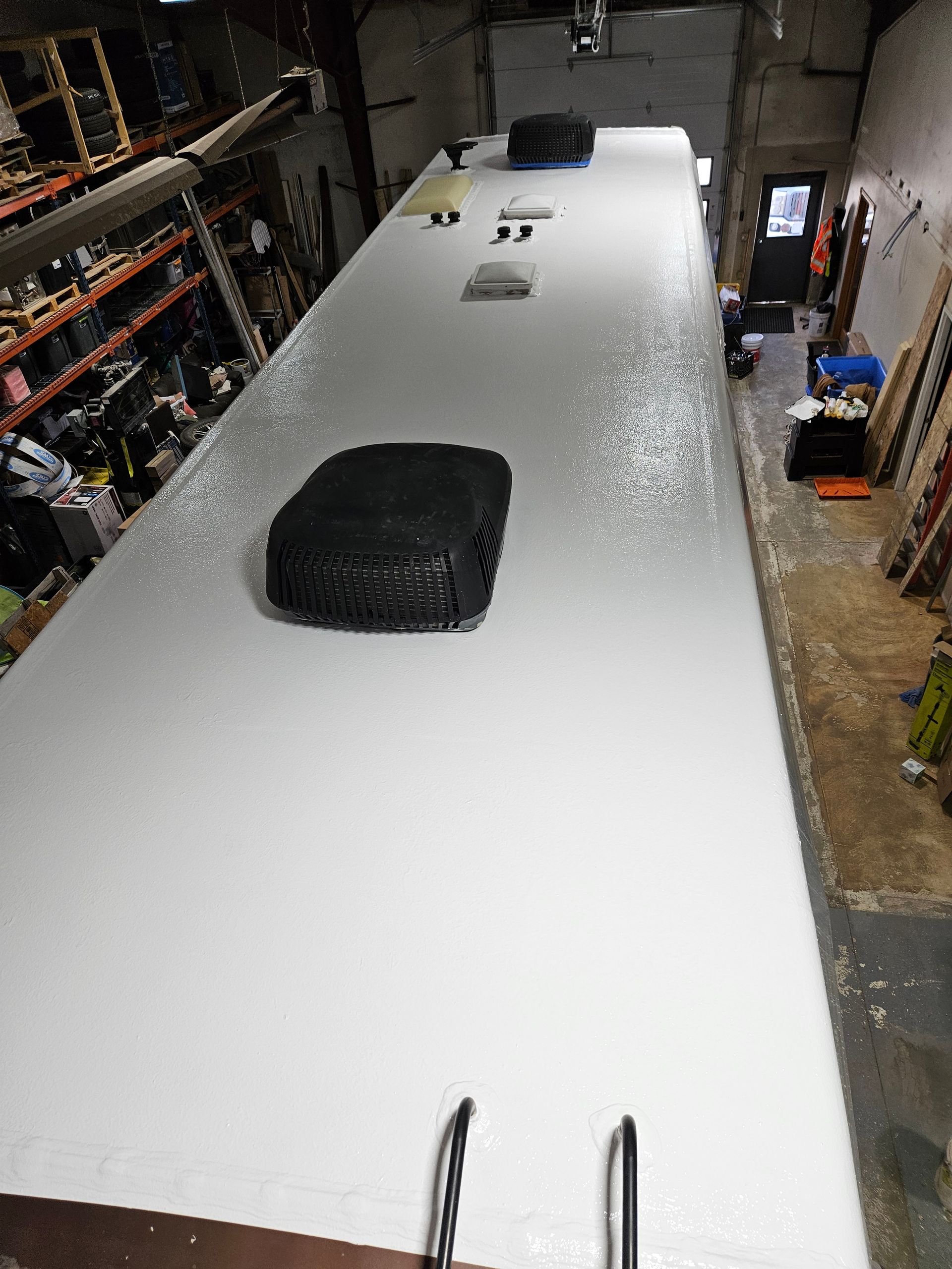 White bus or RV roof seen from above, with black roof vents in a garage or workshop.