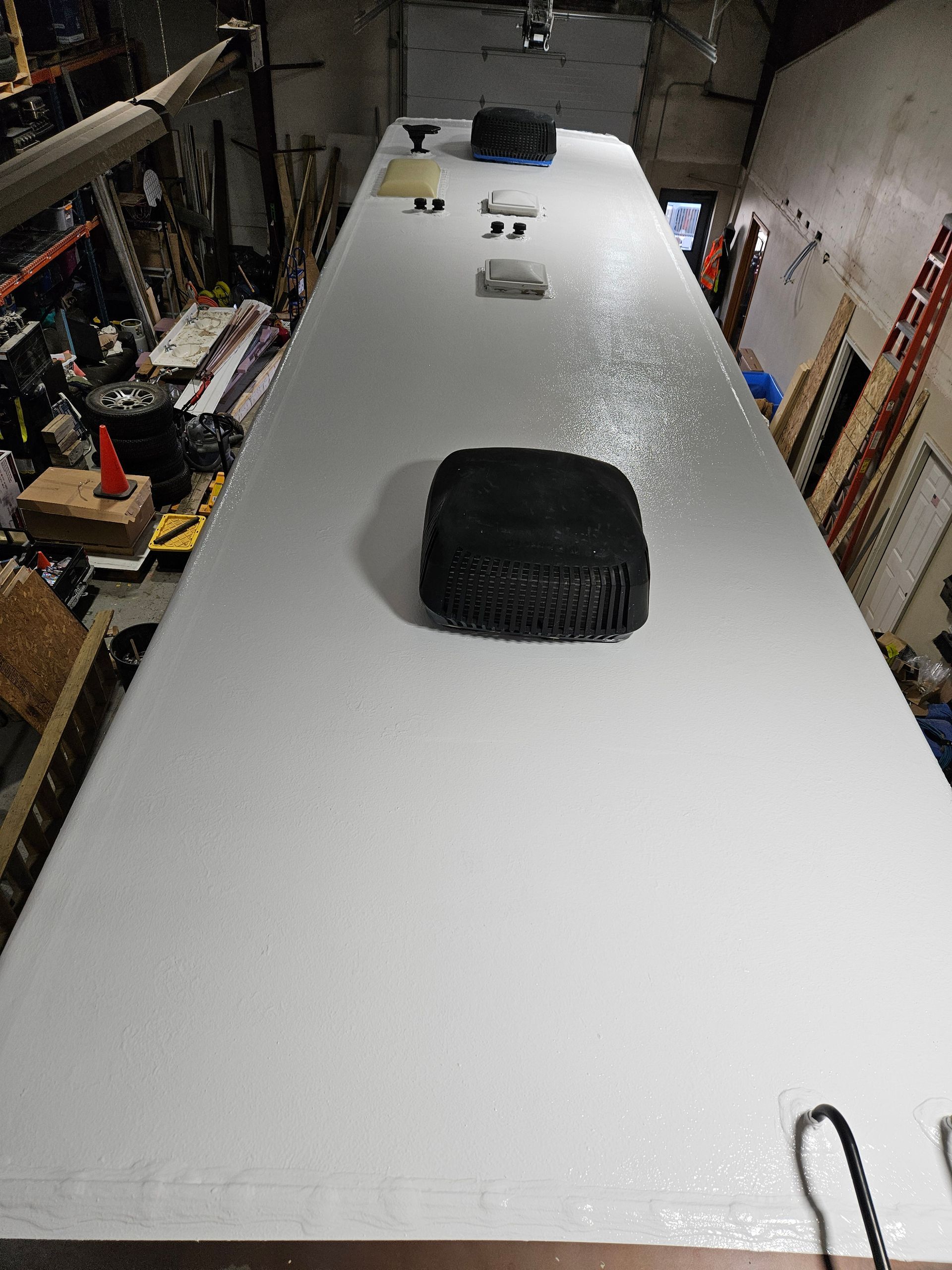 Long white tabletop in a workshop, with tools and a black cushion-like object on top.