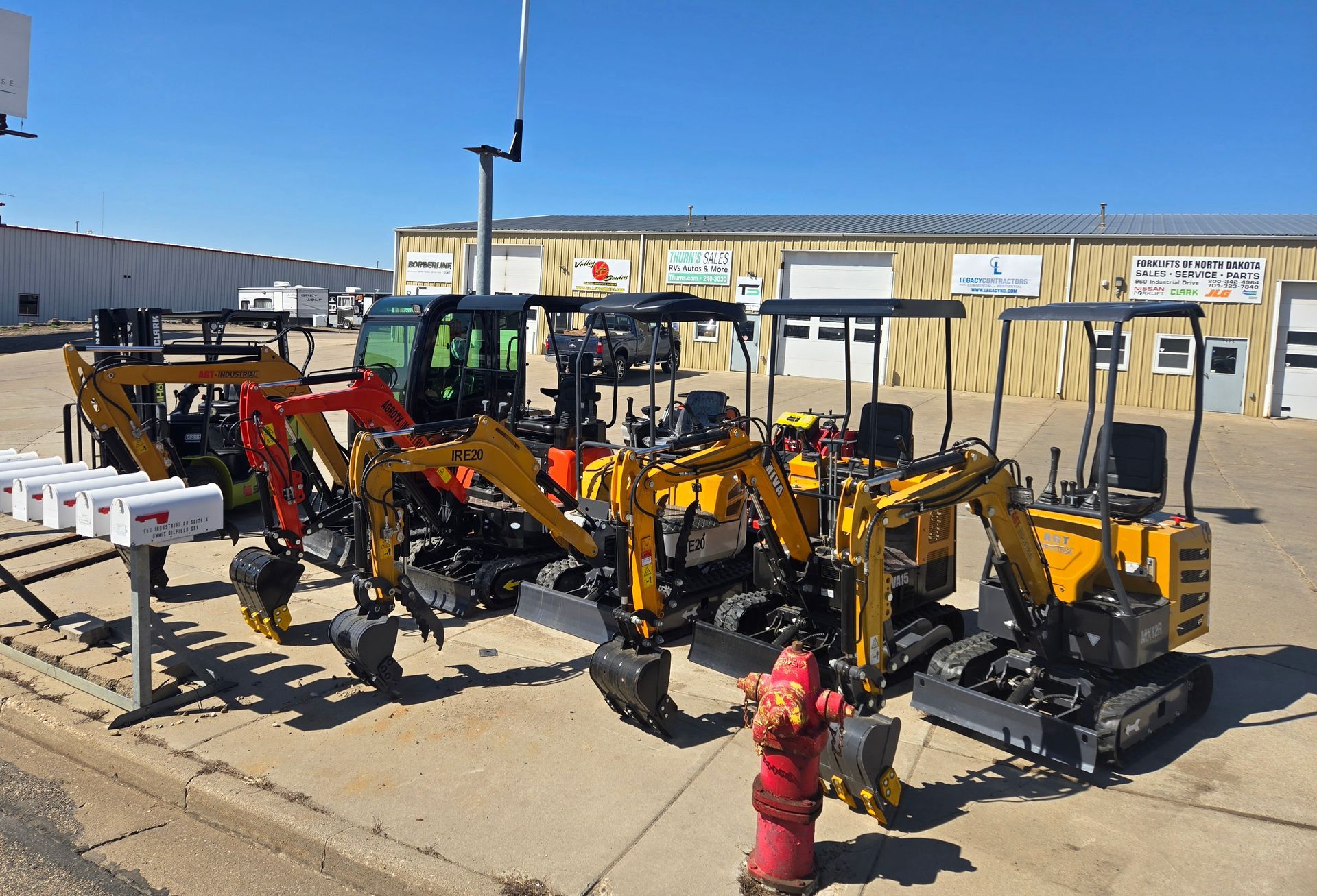 Yellow construction equipment lined up outdoors by a warehouse, with a red fire hydrant in front