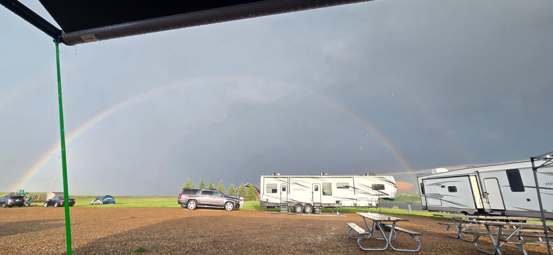 Camper trailers on a gravel lot under a dark sky with a faint rainbow in the distance