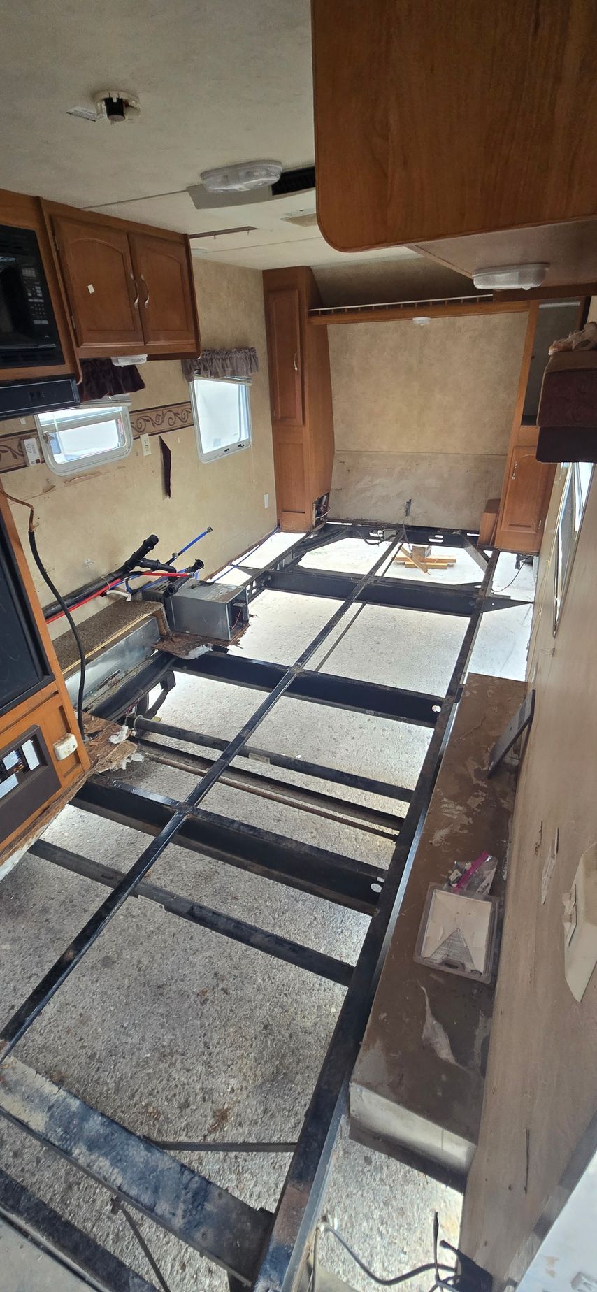 RV interior with a metal bed frame and wooden cabinets, cluttered and partially disassembled