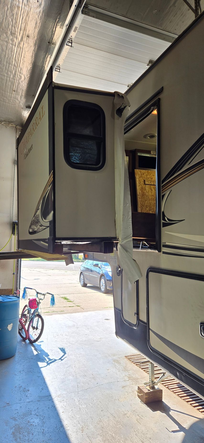 View from between two RVs into a bright campsite, with a blue tricycle and chair on the ground.
