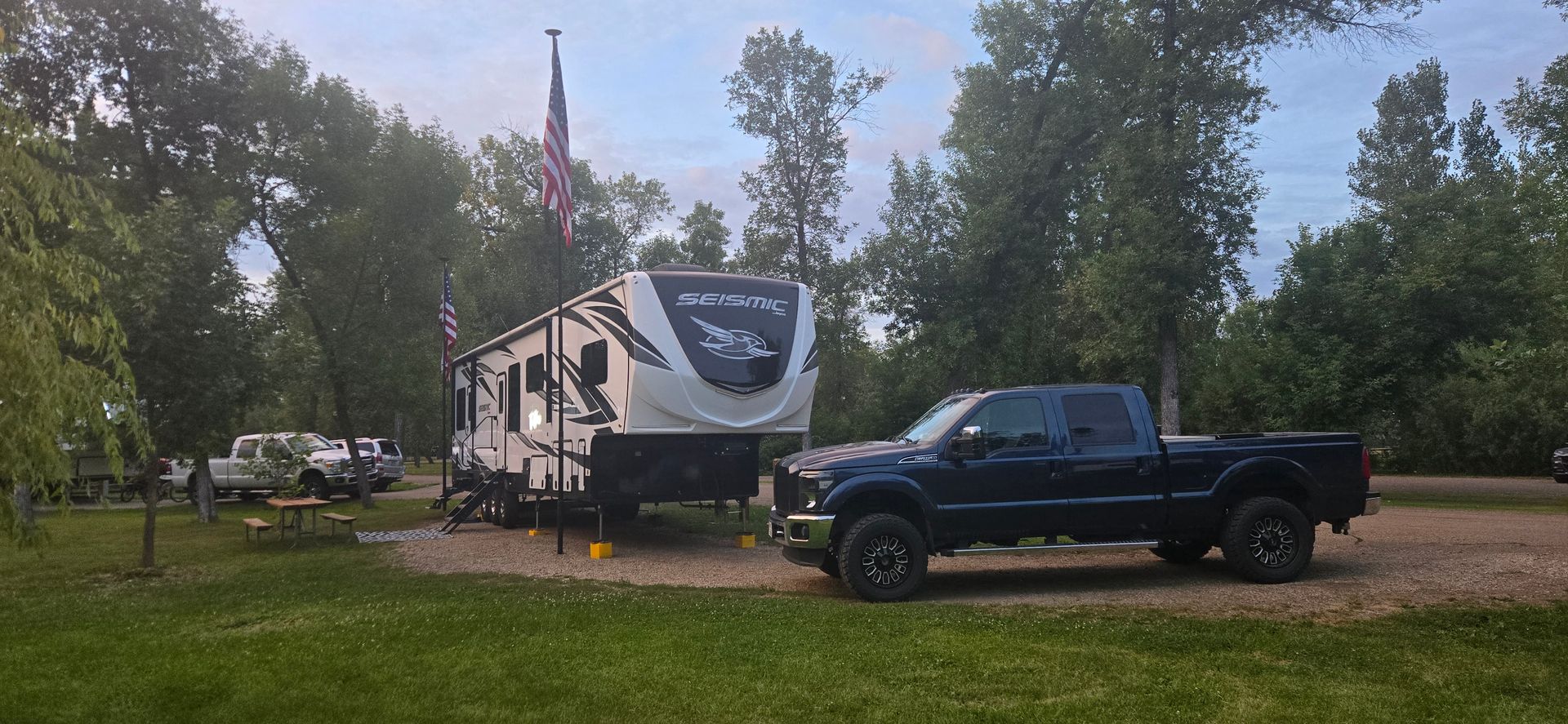 Black pickup truck parked beside a white RV in a grassy campsite under trees