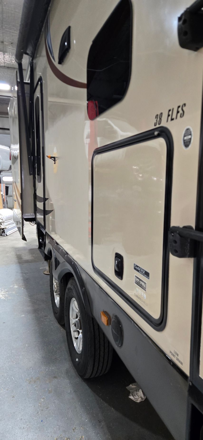 Side view of a beige RV trailer parked in a lot, with a black trim and storage compartment visible.